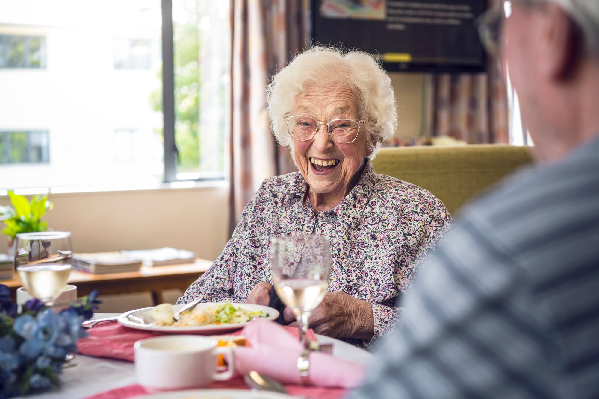 Older woman sitting at table having a meal with older man, looking happy, smiling