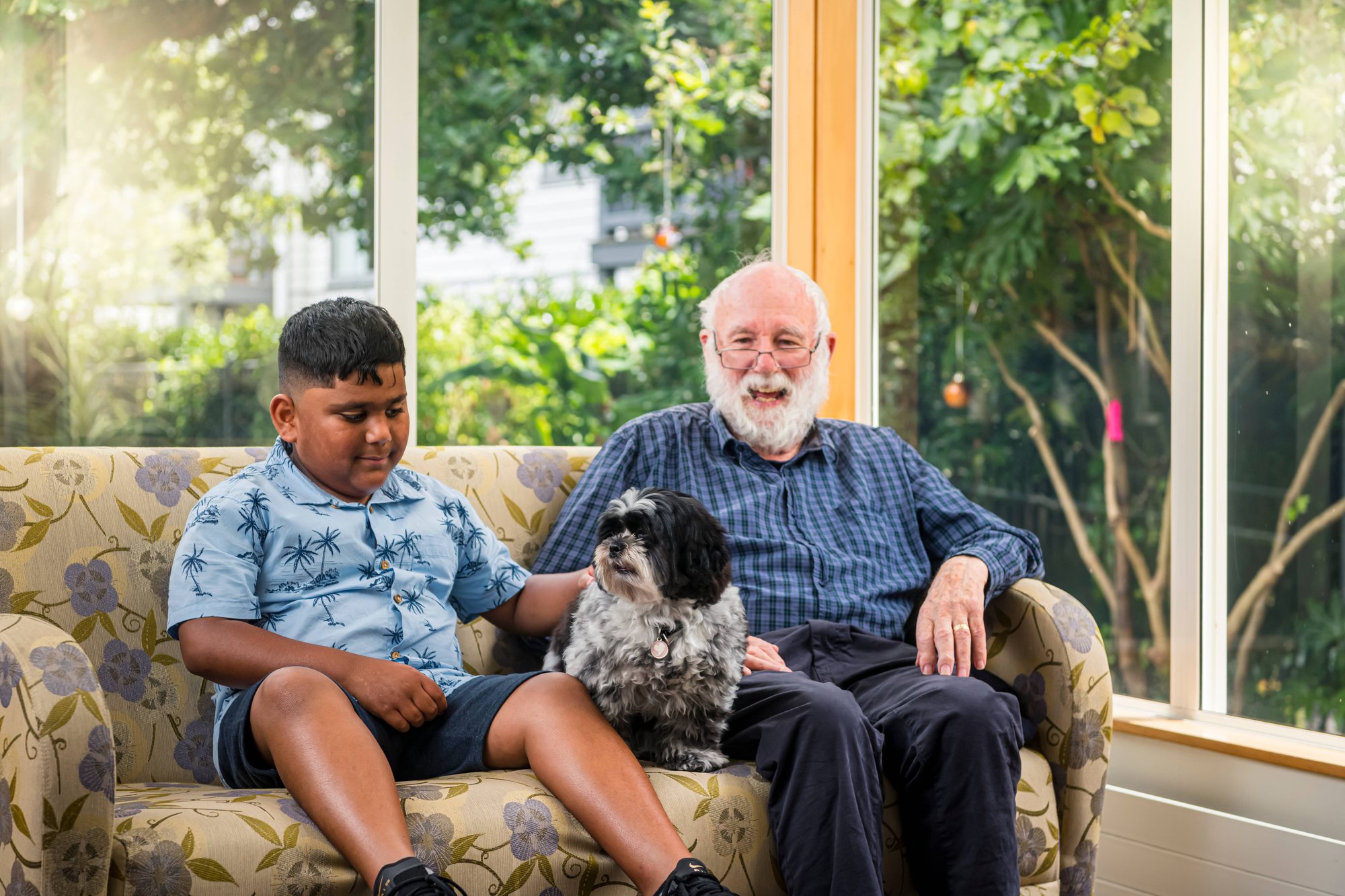 Older man sitting on couch with child and small dog, smiling